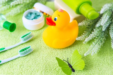 Yeşil havluyla banyo aksesuarları. Lastik ördek, diş fırçası, deniz tuzu, sabun ve losyon. Banyo için bebek bakım aksesuarı. Çocuklar için sarı ördek yavrusu.