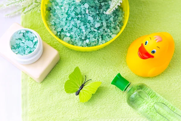 Accessoires de salle de bain sur une serviette verte. Canard en caoutchouc, brosses à dents, sel de mer, savon et lotion. Accessoires de soins pour bébé pour bain. Jouet de canard jaune pour enfants . — Photo