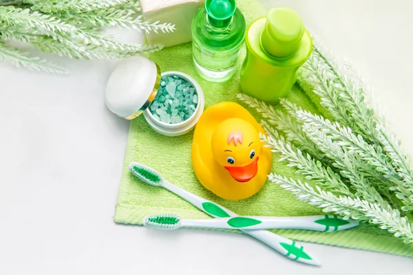 Accesorios de baño en una toalla verde. Pato de goma, cepillos de dientes, sal marina, jabón y loción. Accesorios para el cuidado del bebé para baño. Juguete de patito amarillo para niños . — Foto de Stock