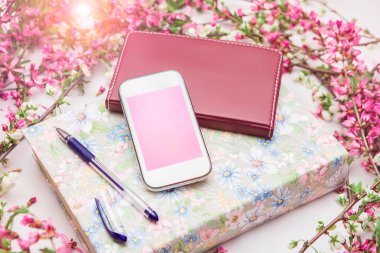 Ofis aksesuarları bir güzel çiçek dallarda beyaz bir arka plan ile. Telefon, defter ve bir kalem bir kitapla.