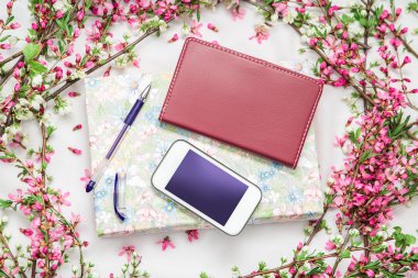 Ofis aksesuarları bir güzel çiçek dallarda beyaz bir arka plan ile. Telefon, defter ve bir kalem bir kitapla.