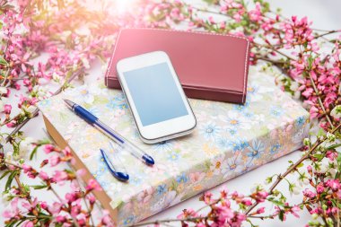 Ofis aksesuarları bir güzel çiçek dallarda beyaz bir arka plan ile. Telefon, defter ve bir kalem bir kitapla.