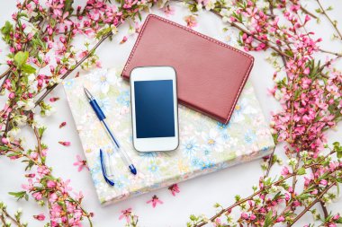 Ofis aksesuarları bir güzel çiçek dallarda beyaz bir arka plan ile. Telefon, defter ve bir kalem bir kitapla.
