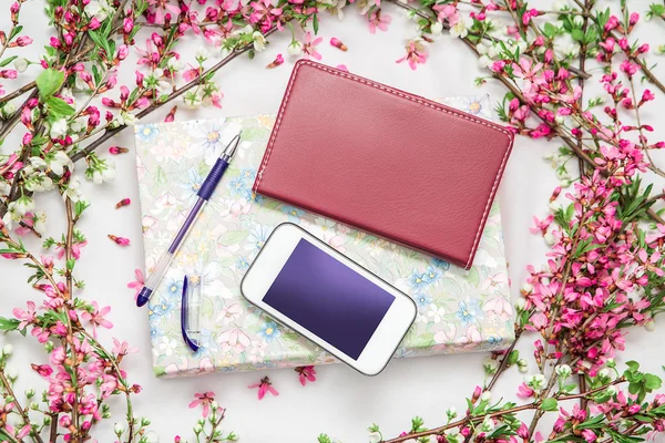 Accesorios de oficina con una hermosa flor ramas sobre un fondo blanco. Teléfono, cuaderno y un bolígrafo con un libro . — Foto de Stock