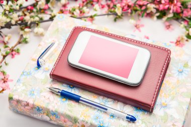 Ofis aksesuarları bir güzel çiçek dallarda beyaz bir arka plan ile. Telefon, defter ve bir kalem bir kitapla.