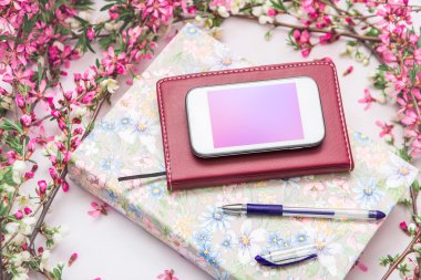 Ofis aksesuarları bir güzel çiçek dallarda beyaz bir arka plan ile. Telefon, defter ve bir kalem bir kitapla.