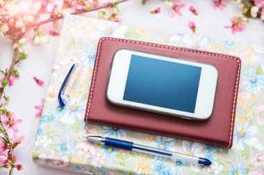 Ofis aksesuarları bir güzel çiçek dallarda beyaz bir arka plan ile. Telefon, defter ve bir kalem bir kitapla.