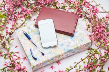 Ofis aksesuarları bir güzel çiçek dallarda beyaz bir arka plan ile. Telefon, defter ve bir kalem bir kitapla.