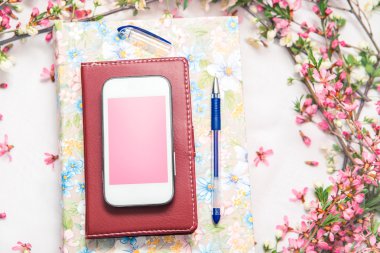 Ofis aksesuarları bir güzel çiçek dallarda beyaz bir arka plan ile. Telefon, defter ve bir kalem bir kitapla.