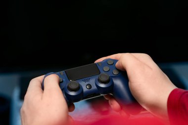 Bir adamın elleri, fotoğrafın ön planında bir konsol kumandasını tutar.