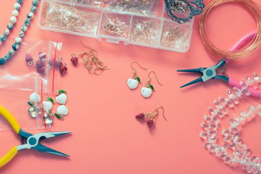 Evde kendi ellerinle mücevher yapıyorsun. Küpe, bilezik, metal aksesuarlardan kolye ve diş mineli, boncuklu, kristalli kolye üretimi. Kerpeten, tel ve bir kutu mücevher, üst manzara.