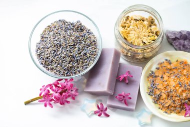 Organik aromatik deniz tuzu, kurutulmuş lavanta ve cam kavanozlarda kasımpatı, ametist kristalleri, beyaz arka planda sümbül çiçekleri.