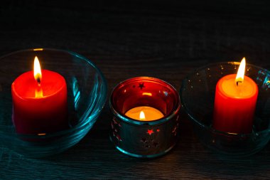 Yakından üç tane kırmızı dekoratif mum. Ev dekorasyonu malzemeleri. Karanlıkta yanan mumların parlak ışığı