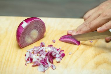 Kesme tahtasında soğan dilimliyorum. Aşçının elleri bıçağı dikkatlice tutuyor ve soğanı kesiyor. Evde yemek pişirmek.