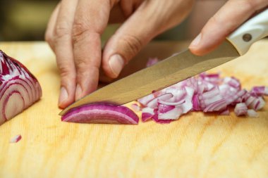 Aşçının elleri bıçağı dikkatlice tutar ve pişirmek için soğanı keser. Yakın planda yemek pişirmek. Sebze dilimliyorum.