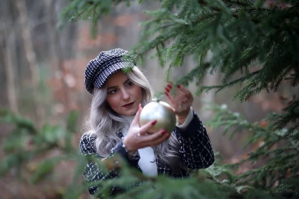 Girl hangs a beautiful Christmas ball on a fir tree in the forest.