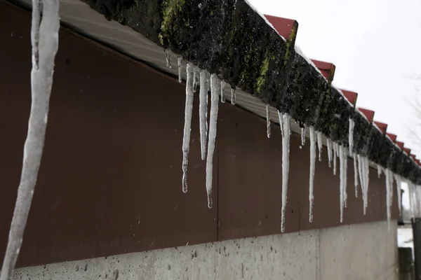 The snow on the roof melts and forms ice icicles.