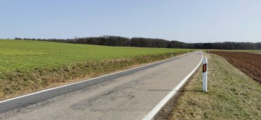 Kırsaldaki çayırların ve tarlaların arasında asfalt yol.