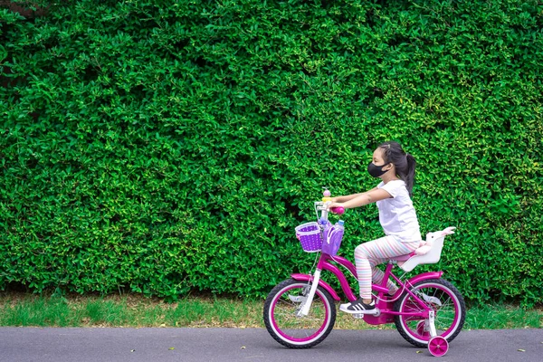 little asian girl wear a mask against PM 2.5 air pollution or disease while ride a bicycle