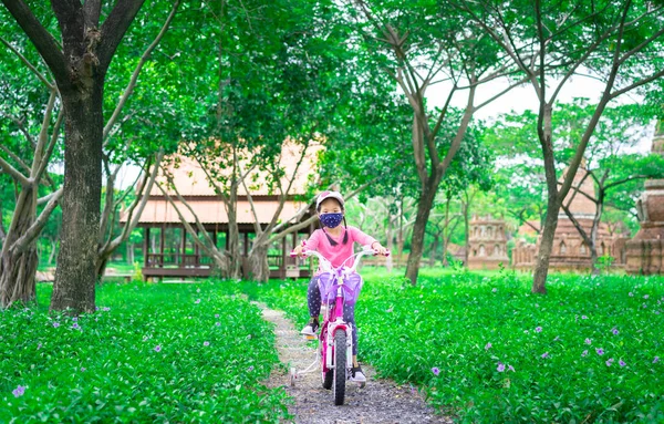 Kleines Asiatisches Mädchen Trägt Eine Maske Gegen Coronavirus Beim Fahrradfahren lizenzfreie Stockbilder