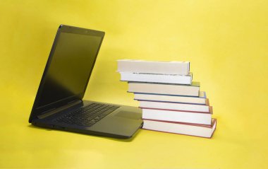 sarı arkaplan üzerine dizüstü bilgisayar ve kitap yığını