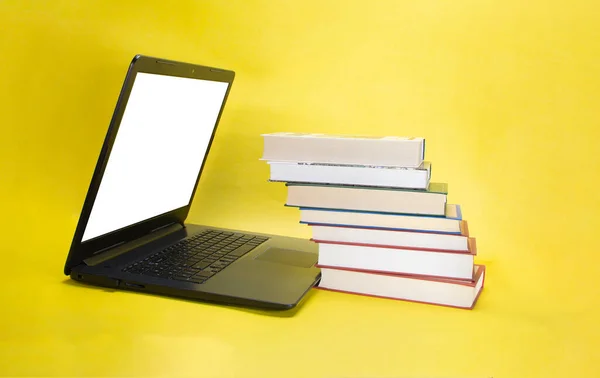 laptop and stack of books on yellow background