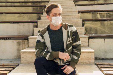 Spor kıyafetli, tıbbi maske takan genç bir adamın portresi. Covid-19 ölçümlerinden dolayı sarı tıbbi maske takan çekici bir erkek model. Beyaz adam kendini korumak için maske takıyor.