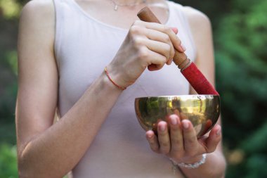 Nilüfer pozisyonundaki kaseden gelen titreşimlerle meditasyon. Doğa yoga temalı eller ve bronz çatal bıçaklar. soul müzik enstrümanında