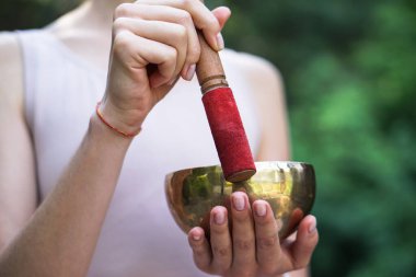 Nilüfer pozisyonundaki kaseden gelen titreşimlerle meditasyon. Doğa yoga temalı eller ve bronz çatal bıçaklar. soul müzik enstrümanında