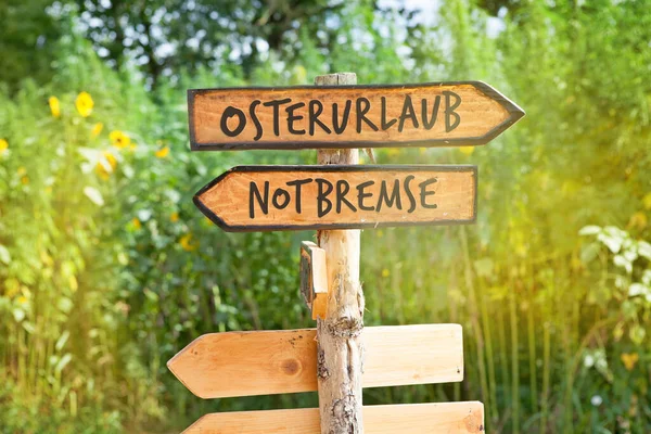 Wooden direction sign with the German words Osterurlaub (Easter holidays) and Notbremse (emergency brake)