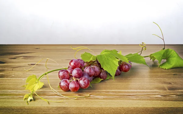 赤ブドウと木製のテーブルの上の葉の束 — ストック写真