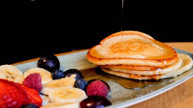 pancakes with fruits and berries on a plate sprinkled with maple syrup
