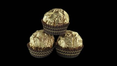 Altın folyo kağıdında bademli üç çikolata topu. Siyah arka plan, Piramit Tarzı Tasarım.