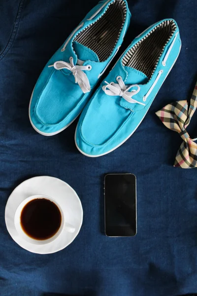 Top view of men`s casual shoes, mobile phone, cup of hot tea and bowtie on jeans background.