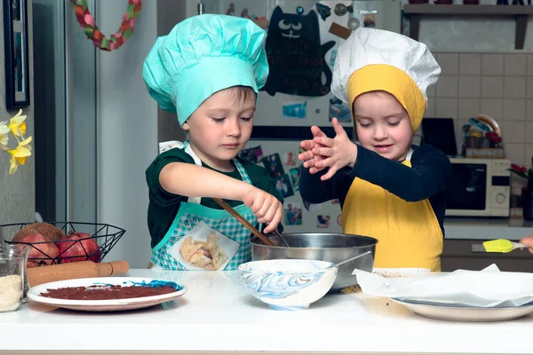 在舒适的厨房里 戴着厨帽和围裙的女孩和男孩都在把粪和勺子混在一起 自由时间活动概念 — 图库照片