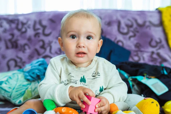 Hüsrana uğramış bir bebek büyük koltukta oturur ve elinde bir oyuncak tutar. Evdeki çocuk.