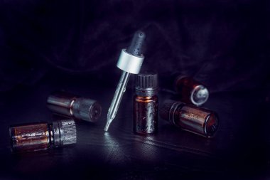 Siyah kapaklı kahverengi cam matara ve siyah arka planda siyah şapkalı cam damlalar. Kozmetik, çiftçilik, kimyasal elementler kavramı.