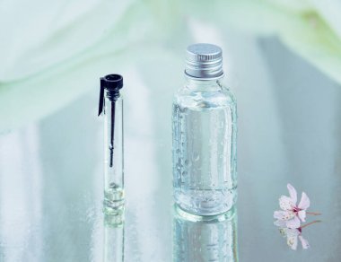 Birinde gümüş kapaklı, diğerinde küçük, siyah kapaklı ve sağında da sulu pembe çiçekli cam mataralar var. Hepsi de su damlalarıyla kaplı ve ıslak yansıtıcı yüzeye yerleştirilmiş. Bitkisel tıp ve kozmetik konsepti.