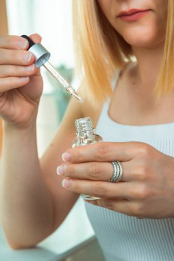 Kozmetik şişesi ve bir kadının elinde bir damla sıvı bulunan cam damlası. Kozmetik malzemeler, aromaterapi ve doğal esanslar..