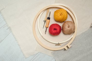 Yuvarlak esneme çerçeveleri, yumruk iğneleri, iplik topları ve beyaz ahşap zeminde üç farklı kumaş düzeni. Yaratıcı işlemeler için araçlar ve ek malzemeler.