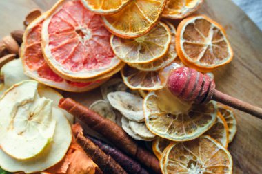 Kurutulmuş meyve dilimlerinin üzerine bal damlatan bal damlatan ballı ballı dipper. Muz, elma, greyfurt, limon ve biraz da meyve şekeri. Hepsi tahta tahtada. Sağlıklı tatlı konsepti.