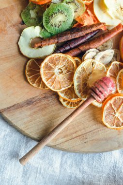 Kurutulmuş meyve dilimleri. Limonlar, kiviler, muzlar, elmalar, meyveli şekerlemeler ve ballı bir ballı şeker. Tahta servis tahtasına serilmiş. Sağlıklı tatlı fikri..