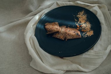 Kuru üzümlü keten ekmeği, kişniş taneleri ve siyah tabakta keten desenler. Altında iki çeşit tuval var..