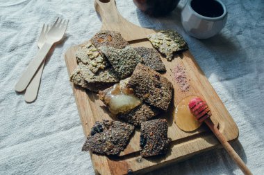 Beyaz keten masa örtüsünün üzerinde keten ekmek, bal, bal ve pembe himalaya tuzu. Arka planda tahta çatallar ve uçan daireler var..