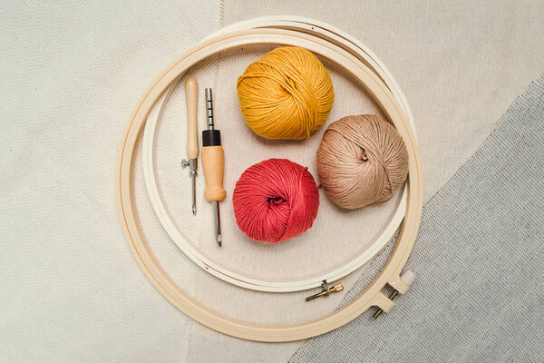 Layout of embroidery hoops, punch needles, balls of yarn on three different types of fabric. Instruments and supplements for creative embroidery.