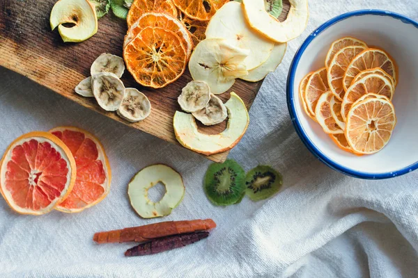 Farklı dokulara yerleştirilmiş dired meyve dilimlerinin üst görüntüsü. Tahta tahta, seramik kase, keten masa örtüsü. Doğal lezzet ve vitamin fikri..