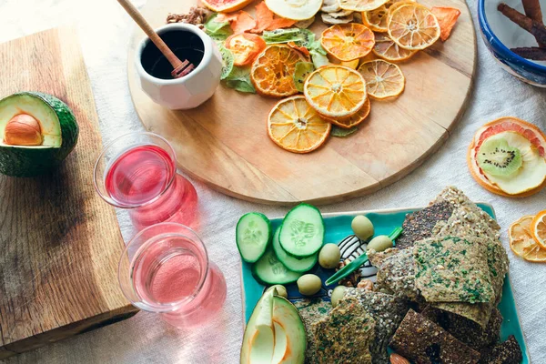 Keten ekmek, taze sebze, kurutulmuş meyve, meyve şekeri ve iki bardak pembe vitamin suyuyla atıştırma tabağı ve panoların yerleşimi. Sağlıklı vejetaryen yemeği fikri.