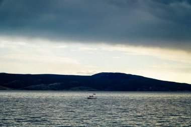 Denizdeki kayık, dağların arka planına karşı. Akşamları deniz suyunun üzerinde fırtına bulutları. 