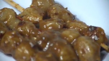 Endonezya usulü leziz ızgara köfteleri kalın fıstık soslu şişler üzerinde servis edin. Ağız sulandıran sokak yemekleri konsepti, beyaz bir tabakta yüksek detay ve iştah açıcı bir yapıyla dönüyor. Mutfak ve yemek blogu için mükemmel.