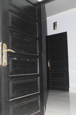 Modern bir evde başka bir odaya açılan açık siyah ahşap bir kapının iç çekimi. Karanlık kapılar, beyaz duvarlar ve parlak döşemeli döşemeler içeren minimalist ev tasarımı. Geçiş kavramı, fırsat, ev iç mimarisi